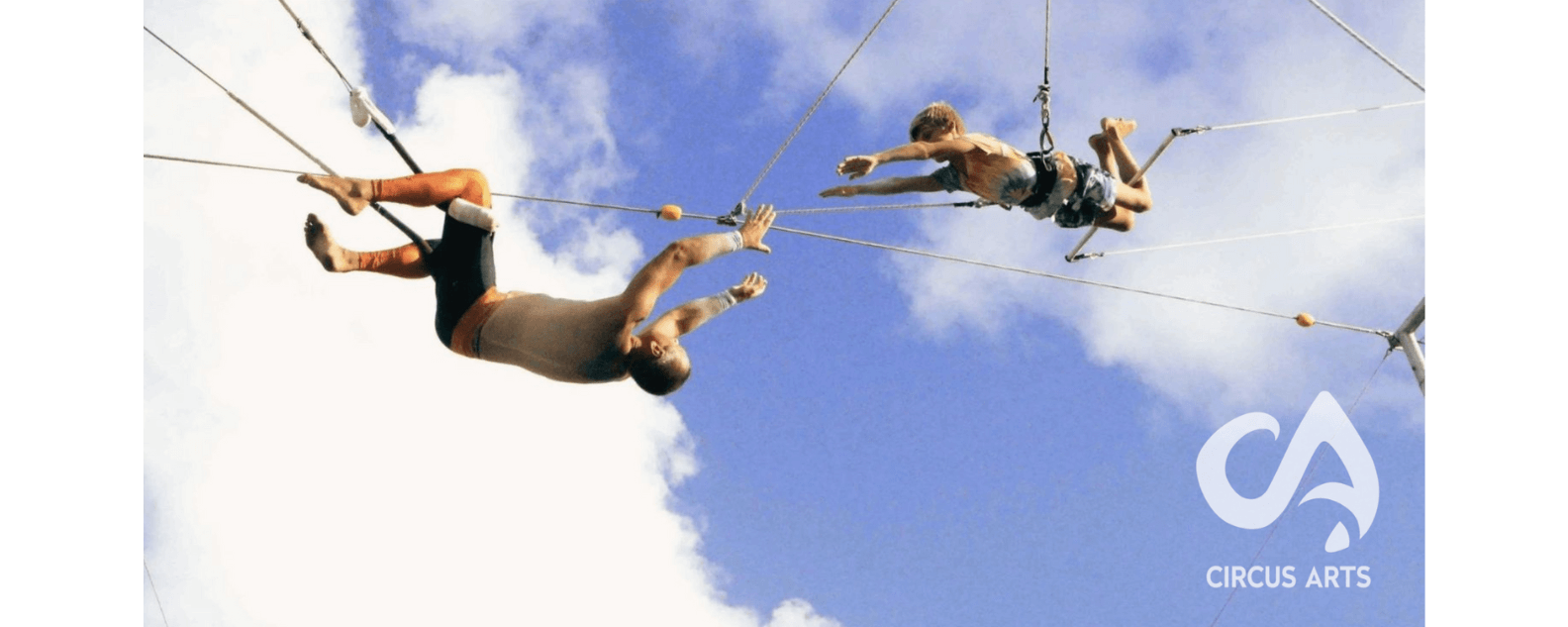 Two people on flying trapeze, sky and clouds in background
