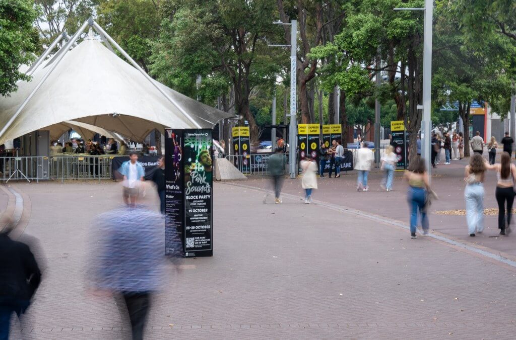 A slightly blurred, eye-level shot shows a paved walkway with people walking in various directions.