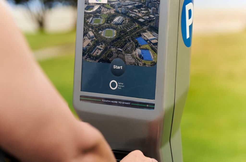 A person is about to touch the screen of a parking meter displaying a map of Sydney Olympic Park.