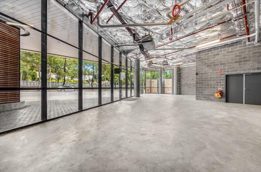 Modern empty commercial space with concrete floor, exposed ceiling and large glass windows.